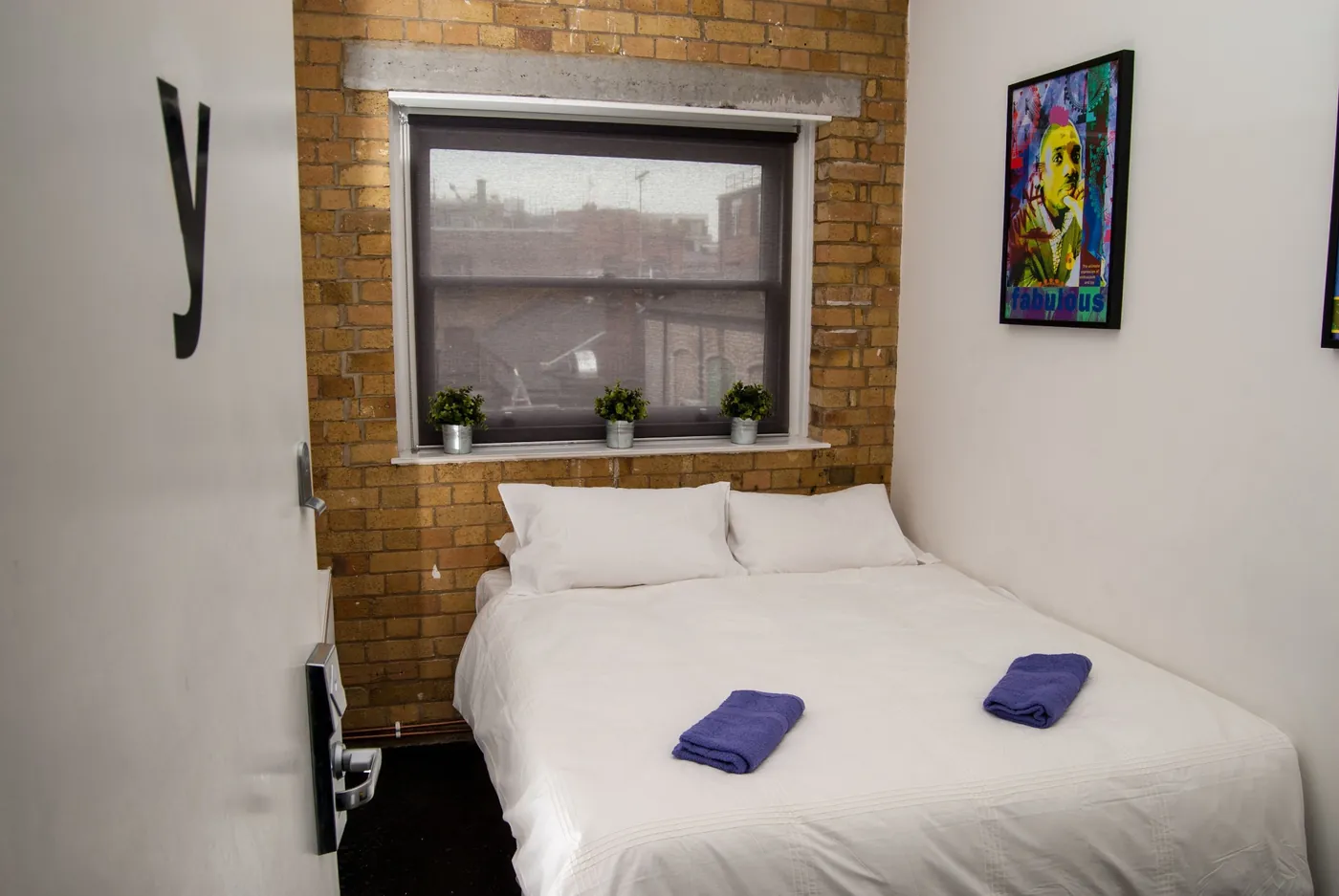 Private double room with an exposed brick wall, a window and folded towels on the bed