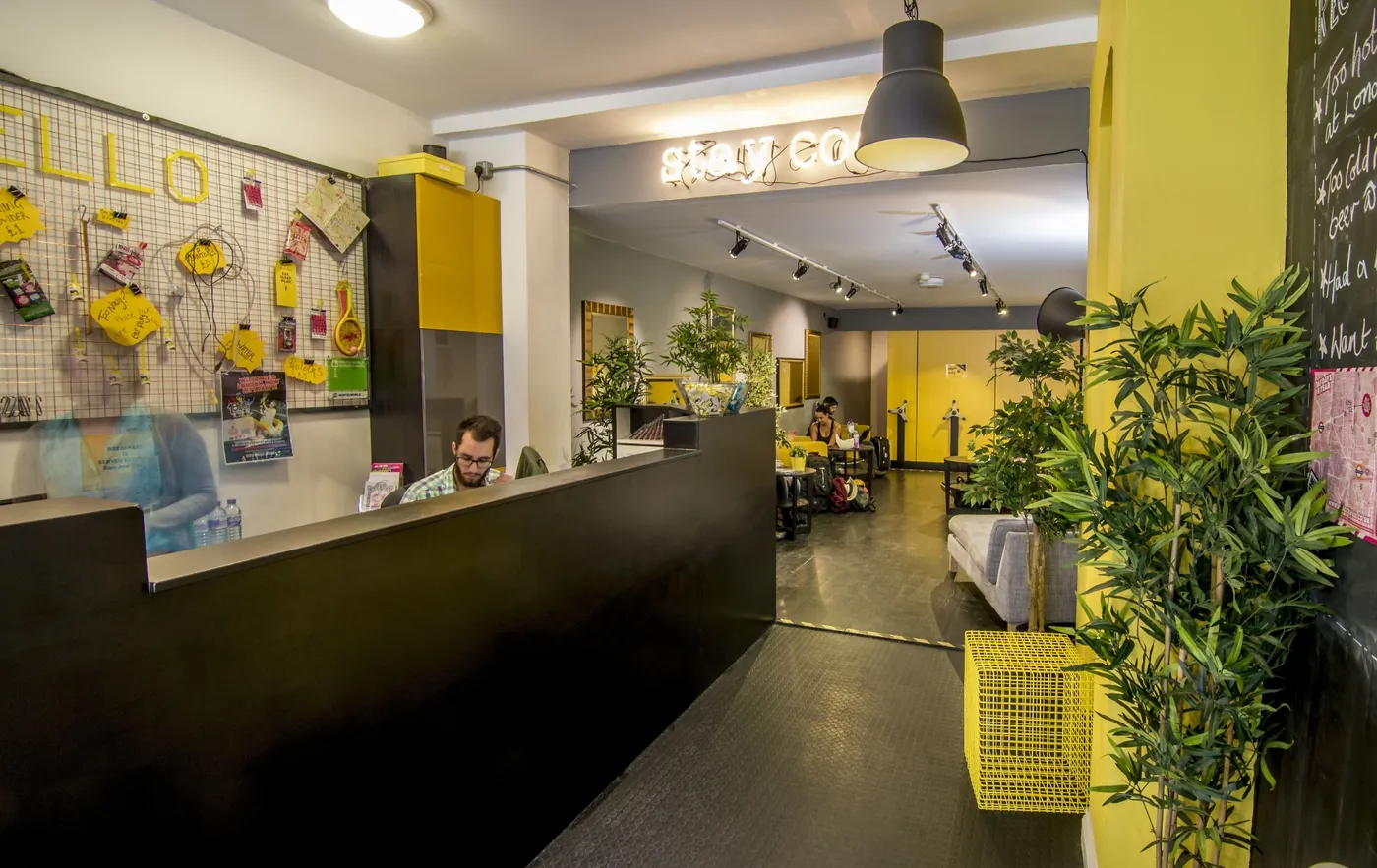 Reception desk in black and yellow, with a pinboard wall, plants and a lounge area beyond